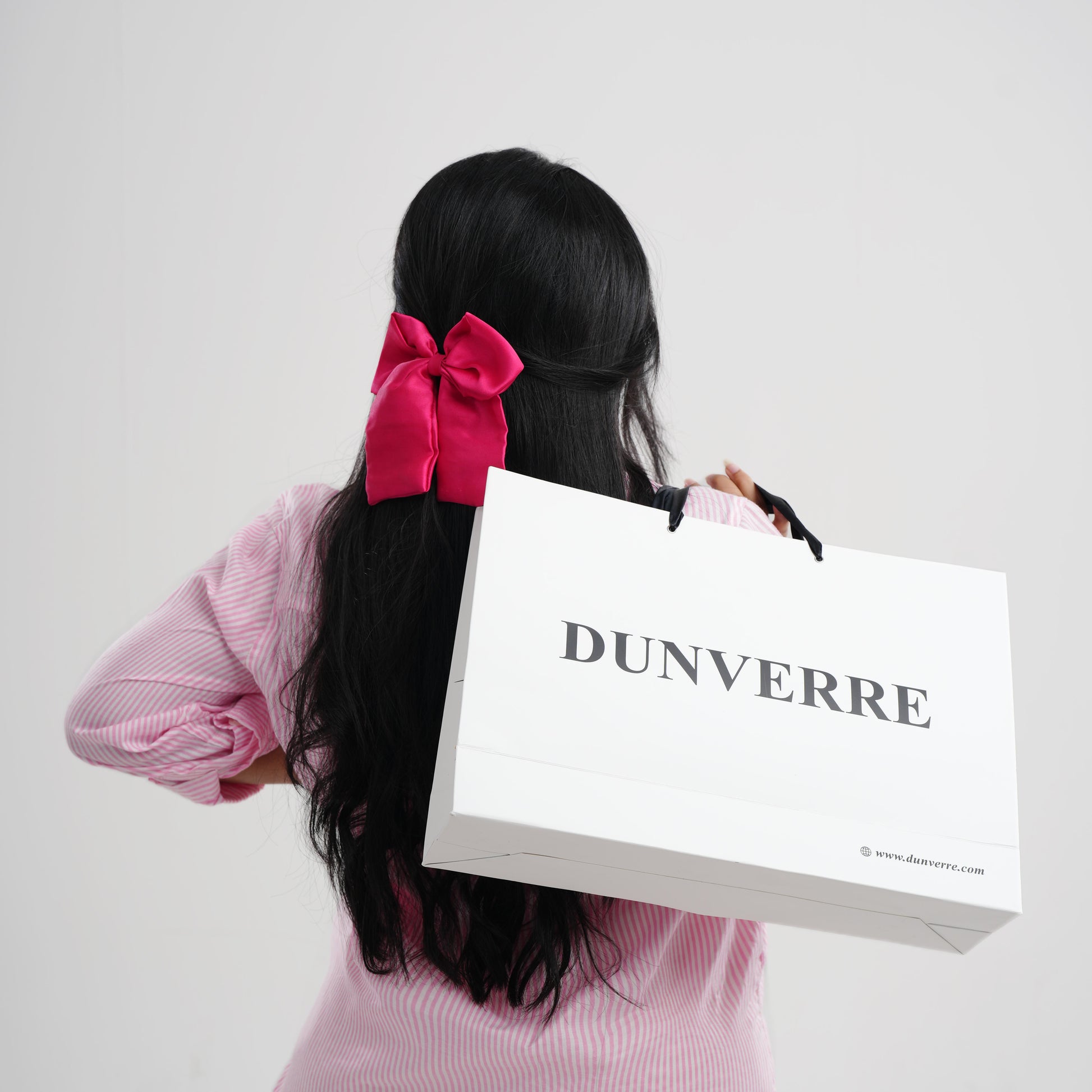Person holding a Dunverre shopping bag with a pink bow in hair